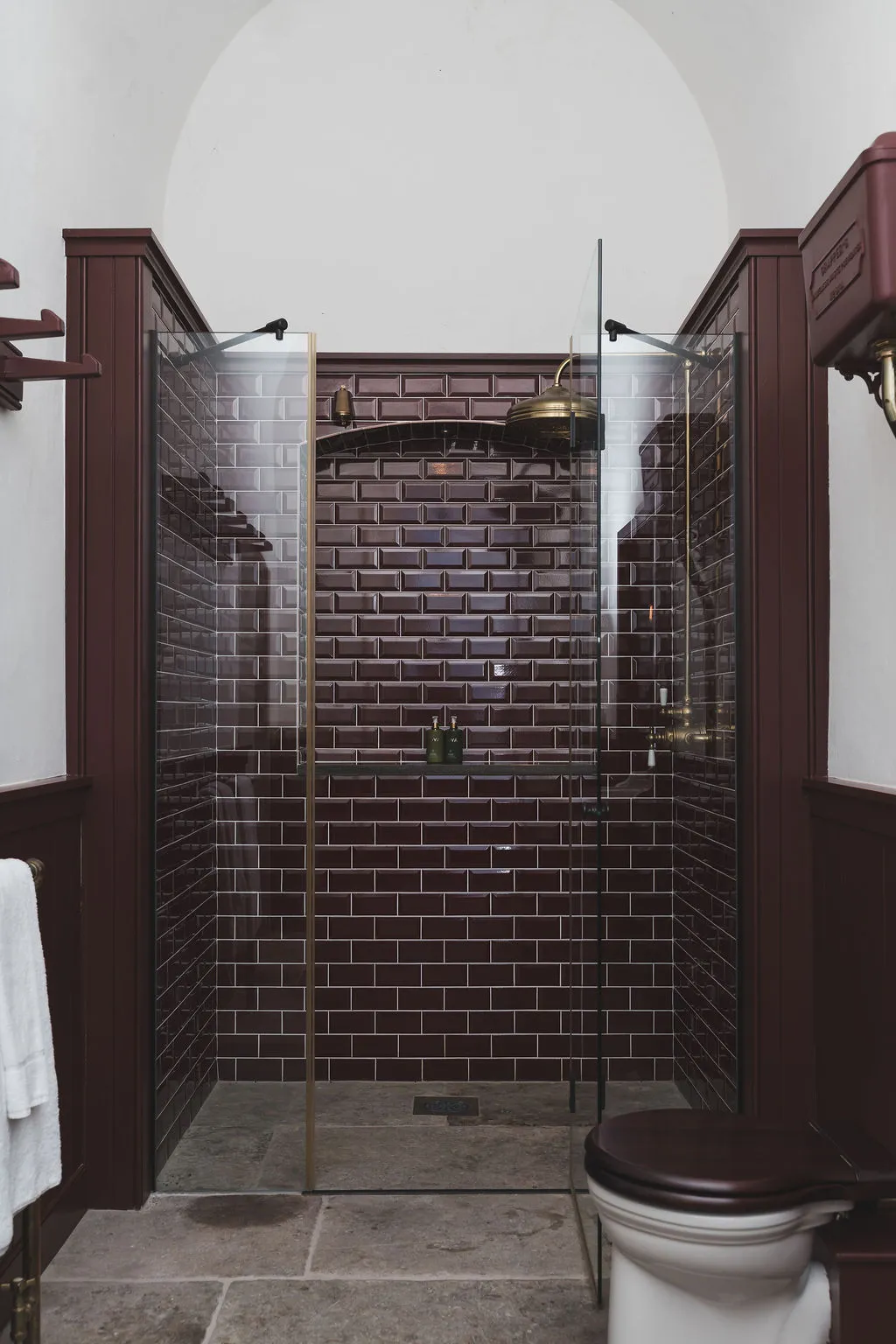 A burgundy-tiled shower room with brass fittings