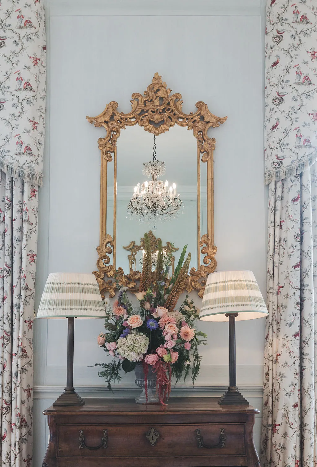 A gilt mirror and striped lampshades on an antique chest