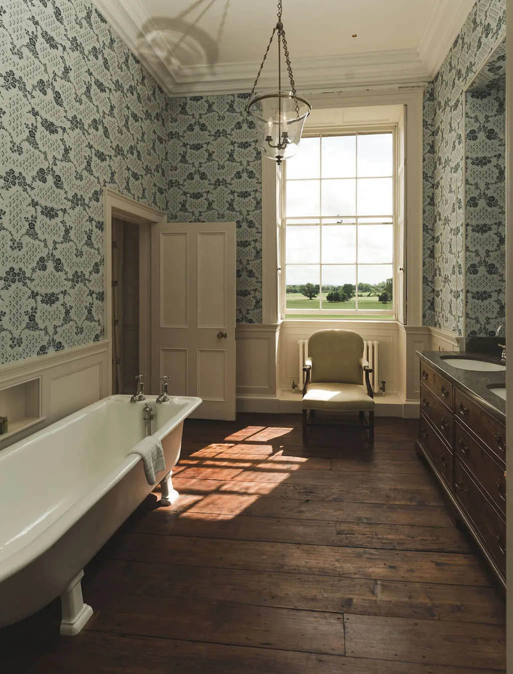 A roll-top bath beneath a sash window, floral papered walls